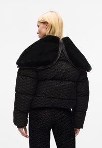 Zwarte pufferjack met een gemêleerd patroon, voorzien van een grote zwarte bontkraag en een ritssluiting. Ontworpen met een cropped silhouet.