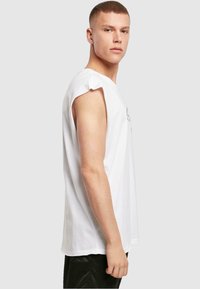 Hvid bomulds ærmeløs t-shirt med en afslappet pasform, let skulderrulning og grafisk design foran; parret med sorte teksturerede bukser.