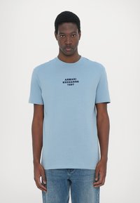 Svetlo modra majica s kratkimi rokavi, izdelana iz bombažne mešanice, z značilnim črnim napisom "Armani Exchange 1991" spredaj, klasičen kroj ovratnika.