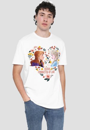 White cotton t-shirt featuring a heart-shaped graphic with two animated female characters, floral accents, and the text "SISTERS CONNECTED BY LOVE."