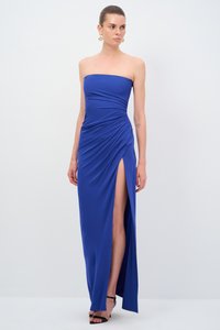 Königsblaues, trägerloses Kleid mit gerafftem Design und einem Schlitz bis zum Oberschenkel, gefertigt aus einem glatten Stoff. Kombiniert mit schwarzen, hohen Sandalen.