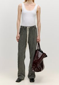 Débardeur blanc ajusté, pantalon rayé noir et blanc avec cordon de serrage, et sac cabas en cuir bordeaux. Des chaussures plates noires complètent la tenue.