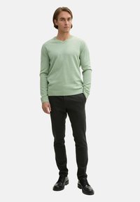 Pulover verde deschis cu decolteu în V, dintr-un material tricotat moale, asociat cu pantaloni strâmți de culoare gri închis și pantofi negri cu șiret. Design simplist și modern.