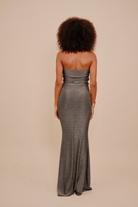 Bezramienna, srebrnoszara suknia wykonana z elastycznej, błyszczącej tkaniny; dopasowany gorset z drapowaną detalą, lejąca się spódnica oraz odkryte plecy.
