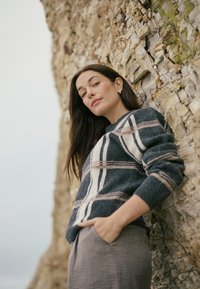 Grauer Wollpullover mit horizontalen blauen und cremefarbenen Streifen, mit langen Ärmeln und lockerer Passform, kombiniert mit einem grauen Rock aus strukturiertem Stoff.