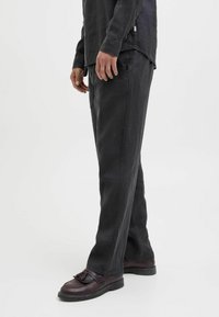 Pantalon noir ample en tissu léger. Caractérisé par un devant plat, des poches latérales et une texture lisse. Porté avec des chaussures foncées.
