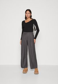 Zwarte langmouwen top met een asymmetrische halslijn, grijze wijde broek met voorplooien en beige schoenen met dikke zolen.