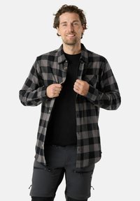 Zwart en grijs geruit flanellen shirt met knopen en een borstzak, gedragen over een zwart t-shirt, gecombineerd met grijze shorts met ritsen.