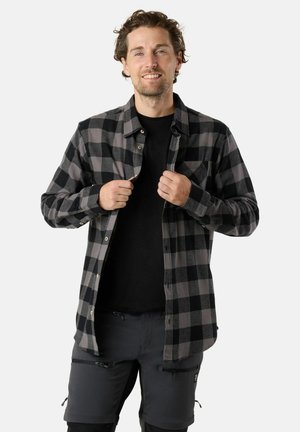 Zwart en grijs geruit flanellen shirt met knopen en een borstzak, gedragen over een zwart t-shirt, gecombineerd met grijze shorts met ritsen.