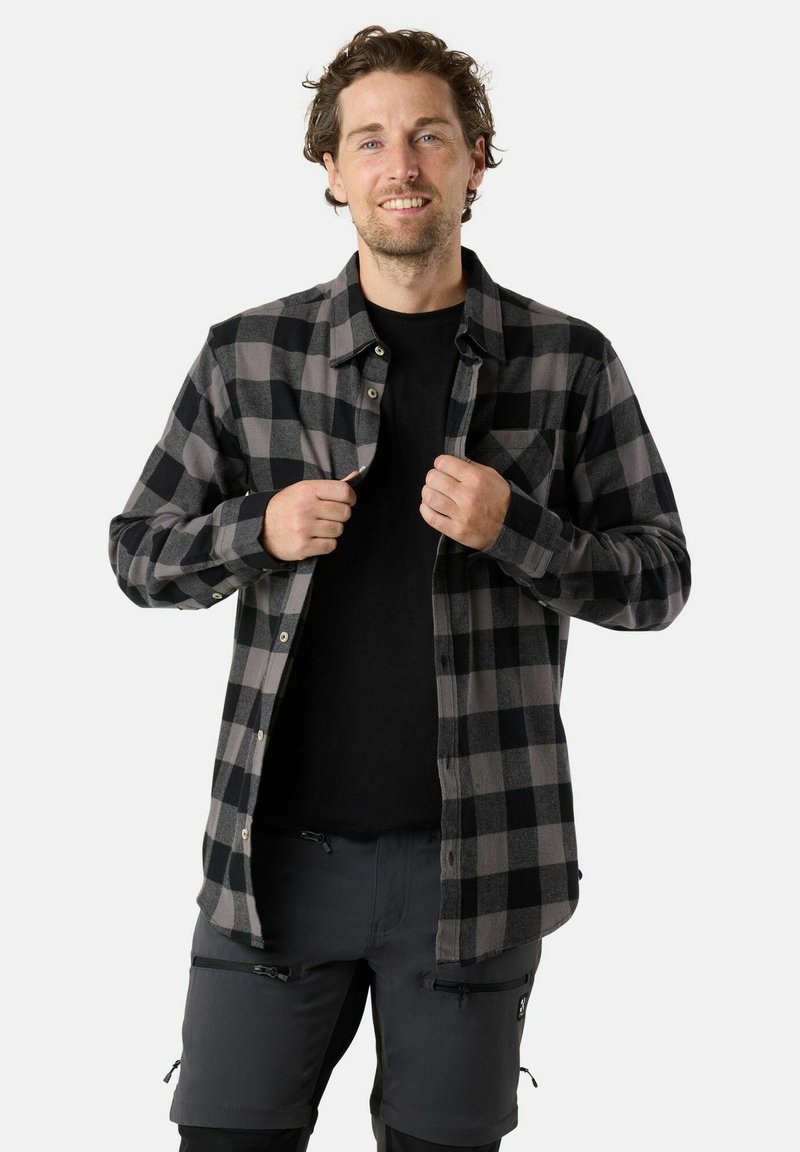 Zwart en grijs geruit flanellen shirt met knopen en een borstzak, gedragen over een zwart t-shirt, gecombineerd met grijze shorts met ritsen.