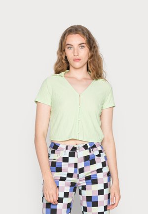 Blusa curta verde-clara com mangas curtas, tecido texturado, decote em V e fecho de botão na parte da frente. Combine com calças coloridas e estampadas.