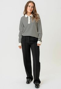 Polo majica dugih rukava sa crno-belim prugama i kragnom, u kombinaciji sa crnim hlačama visokog struka, koje imaju krojeni fit i plisirane detalje.