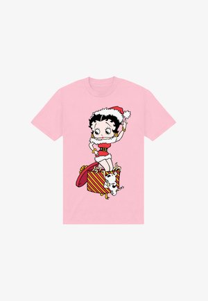 Betty Boop en tenue de père Noël se tient à l'intérieur d'une boîte cadeau rayée de Noël tandis qu'un petit chien blanc saute à côté d'elle.