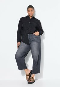 Czarna koszula z guzikami, szare dżinsy o szerokich nogawkach z teksturowanym detalem oraz czarne sandały na platformie z paskiem w leoparda.