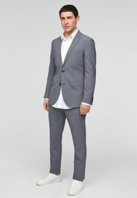 Grijs geruite kostuum met een getailleerde pasvorm, voorzien van een colbert met één knoop en slim-fit broeken, gecombineerd met een wit overhemd en witte sneakers.
