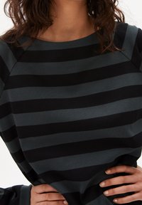 Dlouhý rukáv top v tmavě zelené a černé pruhy. Má kulatý výstřih a texturovanou tkaninu s uvolněným střihem. Bez viditelného kování.
