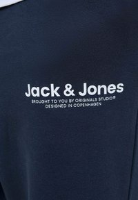Mörkblått tyg med en slät yta har vit tryckt text: "Jack & Jones" och ytterligare varumärkesdetaljer nedanför.