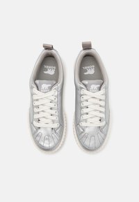 Metallic silver sneakers with white laces and a textured finish. Features a round toe, padded collar, and logo on the insole. Flat rubber sole.