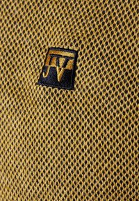 Textured yellow mesh fabric featuring a black embroidered logo, showcasing a geometric pattern with small hexagonal openings.