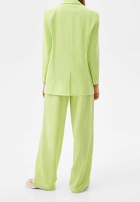 Un costume vert clair avec un blazer ajusté et un pantalon ample. Le tissu semble lisse avec un léger brillant. Le blazer a une fermeture à un bouton et des manches longues.