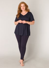 Middengrijzen V-hals tuniek top gecombineerd met donkere leggings en naaktkleurige strappy hakken. Gladde stof met een ontspannen pasvorm en korte mouwen. Eenvoudig ontwerp.