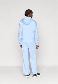 Svetlomodrá mikina s kapucňou a zodpovedajúce tepláky vyrobené z mäkkého materiálu. Obsahuje voľný strih a elastické manžety. Čierne športové topánky dopĺňajú vzhľad.