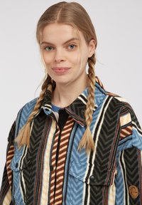 Multicolored flannel jacket featuring a zigzag pattern in blue, black, brown, and cream; two chest pockets and button closures.