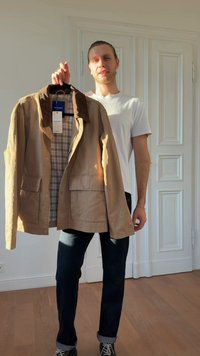 Gombos bezárású khaki dzseki, két első zsebbel, kordbársony gallérral és kockás béléssel, egy emberen tartott vállfán lógva.