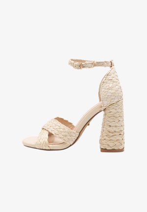 Austītu dabisko šķiedru augstpapēžu sandales ar platu pītā siksnu pāri pirkstiem un potītei, ar biezām raupjām papēža daļām. Krāsa: bēša.