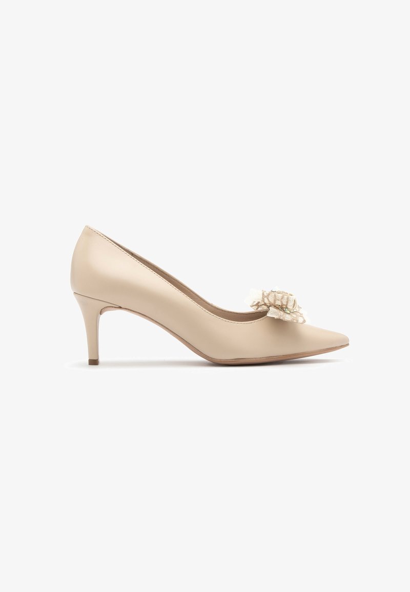 Bež lakirana usnjena visoka petka s koničastim prstom, ki ima čipkast cvetlični detajl na zgornjem delu. Petka dolga približno 7,5 cm.