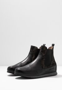 Botas negras hasta el tobillo con punta de cuero suave, detalles en piel de serpiente texturizada, paneles laterales elásticos y suela plana de goma. Marca sutil en el lateral.