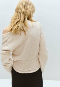 Suéter liviano rosa claro con escote off-shoulder en tejido de punto, con dobladillo y puños acanalados. El diseño presenta un ajuste relajado y un detalle texturizado.