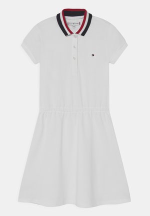 Biała sukienka polo z krótkim rękawem, z kołnierzykiem w czerwone, białe i granatowe paski, trzema guzikami, elastyczną talią oraz małym logo Tommy Hilfiger na piersi.