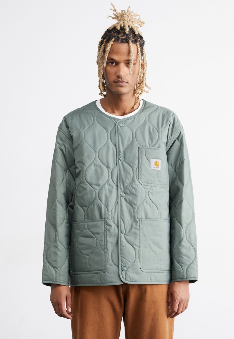 Quilted grüne Jacke mit abgerundeten Kanten, strukturiertem Muster, Druckknöpfen und einer Vordertasche mit einer Logo-Patch. Bequemer Sitz.