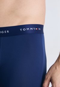 Boxers en bleu marine avec un design ajusté, présentant une ceinture élastique avec logo affichant "TOMMY HILFIGER" en texte blanc.