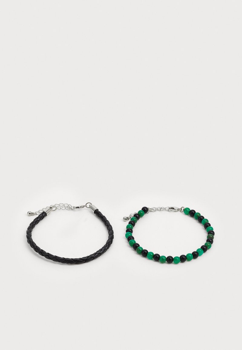 Kaksi ranneketjua: yksi musta punottu nahkaranneke hopeisilla yksityiskohdilla, toinen helmistä koostuva malli, jossa on vihreitä ja mustia kiviä.