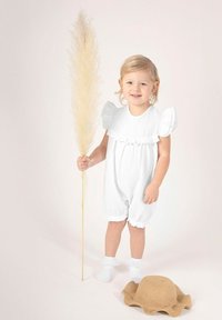 Biały teksturowany kombinezon z falbanowymi rękawami, stojące dziecko trzymające wysoki suchy łodygę trawy. Obok na ziemi leży słomkowy kapelusz.