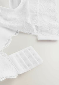 Weiße Unterwäsche mit zarten Spitzenakzenten, einer glatten Stoffstruktur und einem Häkchen- und Ösenverschluss mit mehreren Anpassungsoptionen.