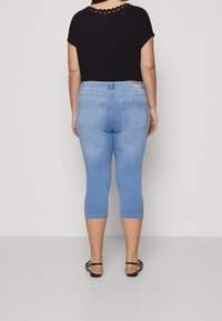 Černý top s výstřihem do tvaru vlnky, který je spojený se světle modrými, ke kolenům sahajícími capri džíny s klasickým pěti kapsovým designem a poutky na pásek.