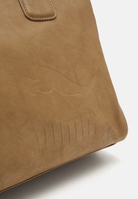 Torebka tote w kolorze tan, z wytłoczonym logo i nazwą marki Puma, o gładkiej fakturze i przeszywanych detalach na uchwycie.