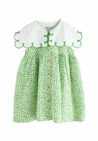 Grön blommig klänning med vit vågformad krage, som har grön kant och små knappar framtill. Tillverkad av lätt, mönstrat tyg.
