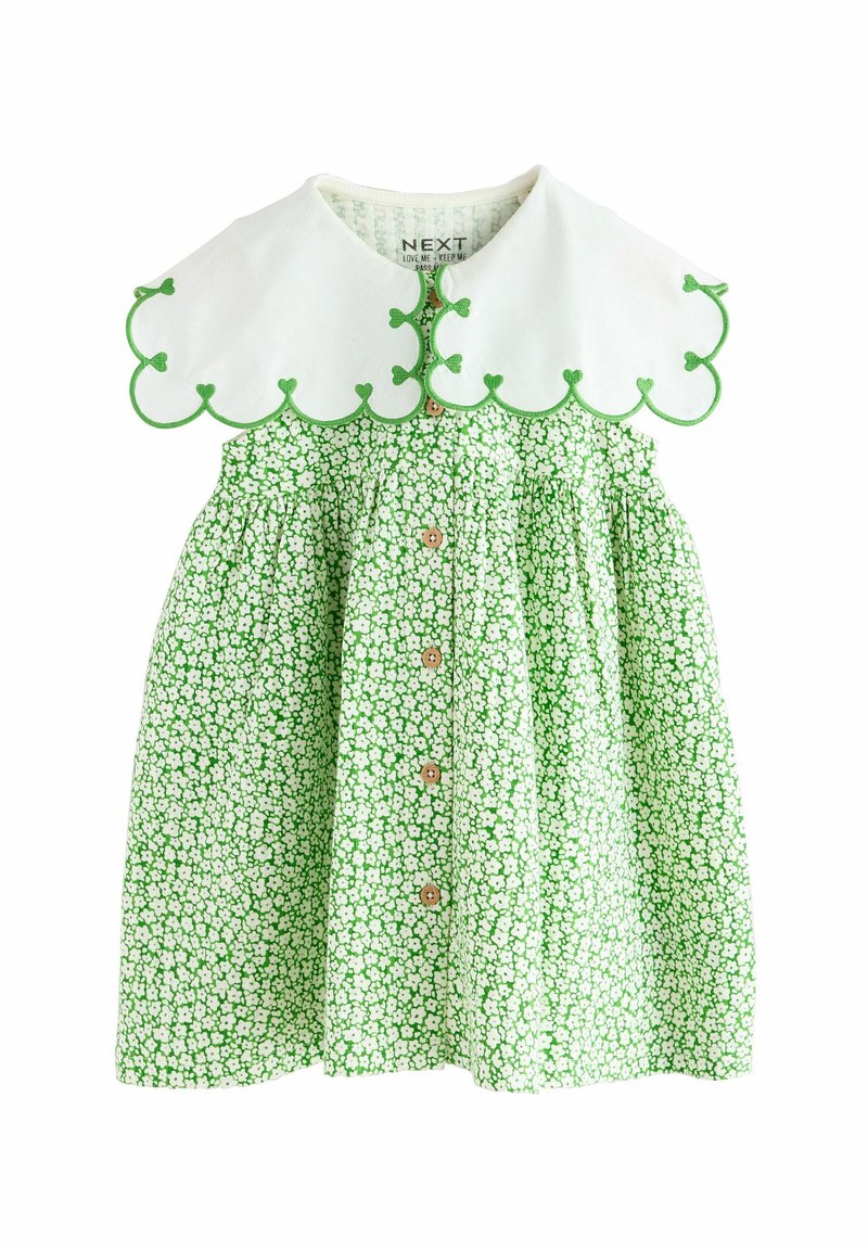 Grön blommig klänning med vit vågformad krage, som har grön kant och små knappar framtill. Tillverkad av lätt, mönstrat tyg.