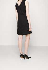 Černé bezramínkové šaty se střihem do tvaru V na zádech, vyrobené z hladkého materiálu. Nosené s černými lodičkami na vysokém podpatku, které zvýrazňují elegantní siluetu.
