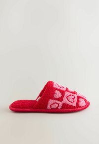 Červená plyšová papuča s ružovými srdcovými vzormi, otvoreným zadným dizajnom a mäkkou textúrou. Má obrysové okraje a pohodlnú, vycpanú podrážku.