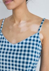 Blue and white gingham top with thin straps, a V-neckline, and scalloped lace trim along the edge, showcasing a checkered pattern.