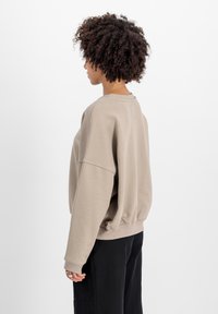 Sudadera de color beige claro con un corte holgado, mangas anchas y ribete en el dobladillo. Presenta una tela texturizada y una pequeña etiqueta en el escote.