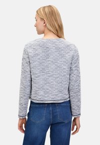 Grijze gebreide trui met lange mouwen, ronde halslijn en cropped lengte, gecombineerd met blauwe spijkerbroek. De achterkant toont de naaddetails.