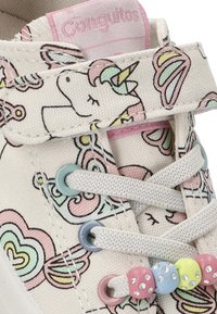 Zapatilla de lona con base blanca, que presenta un colorido patrón de mariposas y unicornios. Incluye detalles en hardware en rosa claro y azul.