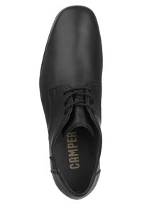Chaussure en cuir noir avec un bout rond, fermeture à lacets, surface lisse et branding subtil sur la semelle intérieure. Design minimaliste et texture.