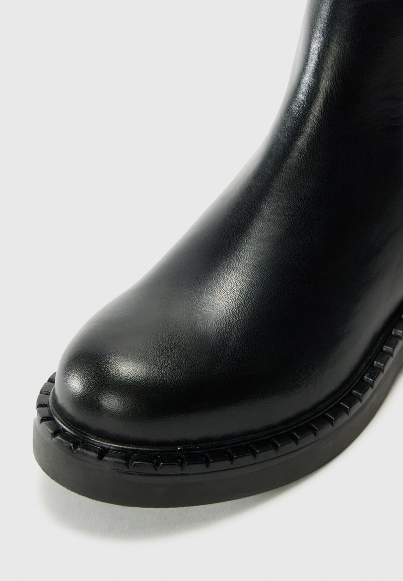 Schwarze Leder-Stiefelette mit runder Zehenpartie, strukturiertem Obermaterial und einer kontrastierenden rutschfesten Sohle. Gestickte Details am Knöchel.